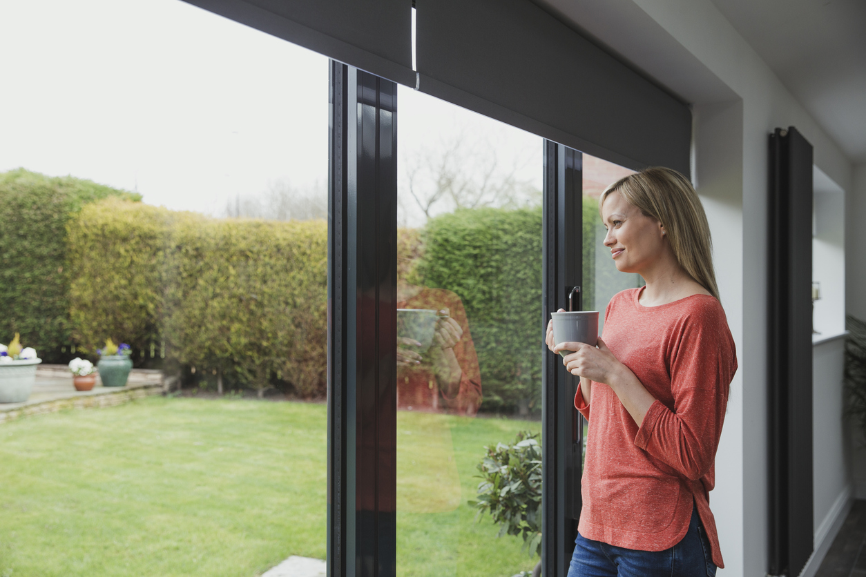 Femme devant une porte-fenêtre coulissante en aluminium noir donnant sur le jardin