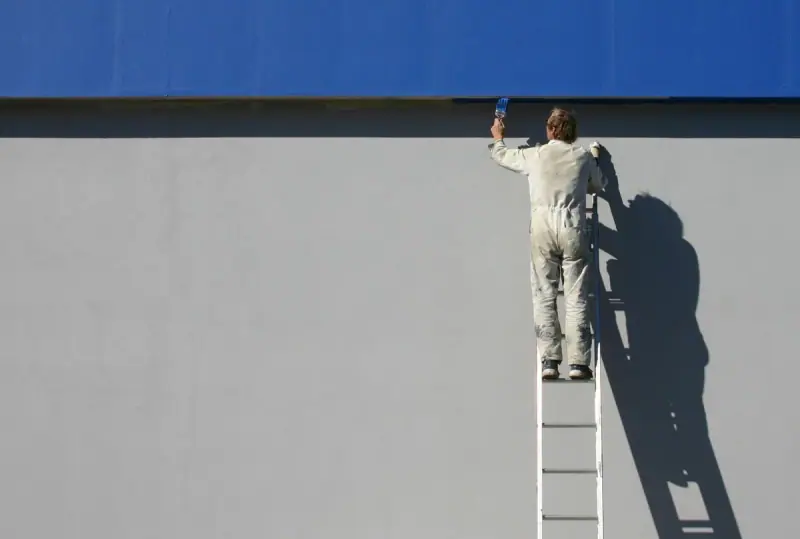 Peintre en bâtiment appliquant une peinture de façade depuis une échelle